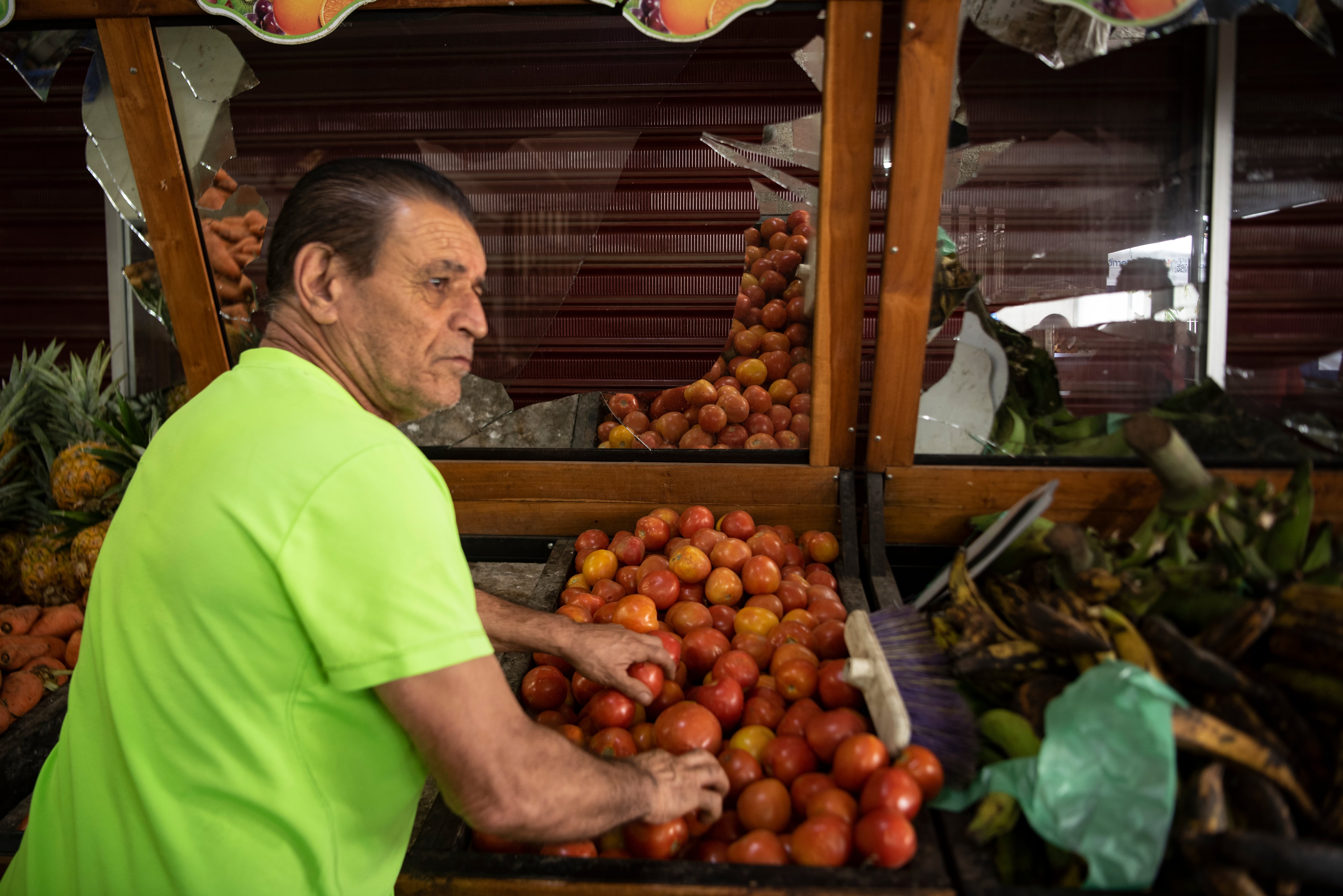 Un hombre escoge tomates en medio de las estanterías rotas de un mercado afectado por una de las explosiones.