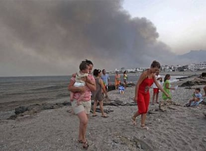 Un grupo de personas abandona la playa de Mojácar con las llamas al fondo.