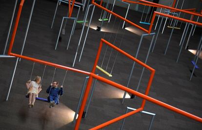 Dos personas montan en columpios que forman parte de la nueva instalación 'One Two Three Swing!' hecho por el colectivo danés SUPERFLEX, en el museo Tate Modern de Londres (Reino Unido).