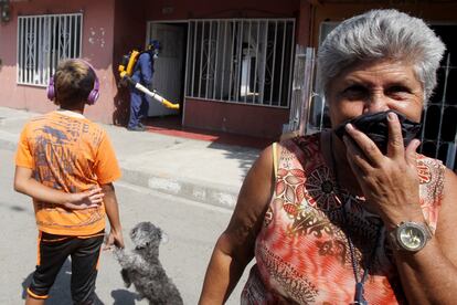 Un grupo de habitantes de la ciudad colombiana de Cali se cubren la boca mientras miembros de la Secretaría de Salud de esa ciudad fumigan algunas viviendas.