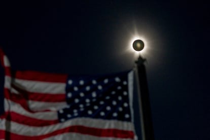 A total solar eclipse is seen beside a waving American flag in Houlton, Maine