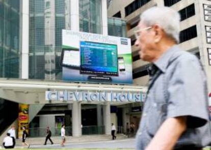 Un hombre camina junto a una pantalla que muestra la información de la bolsa en Singapur.