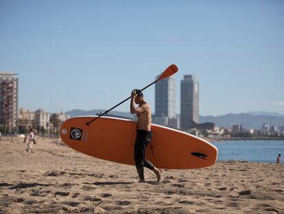Un hombre sale el martes con su tabla de surf de la playa de Barcelona.