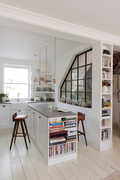 Una de las paredes de la cocina se ha convertido en ventana interior para llevar luz natural hasta la escalera. La isla central funciona como barra para comer y estantería, y además esconde el lavabo del gato de la dueña. Las lámparas de techo son de Nud y los taburetes fueron adquiridos en eBay.