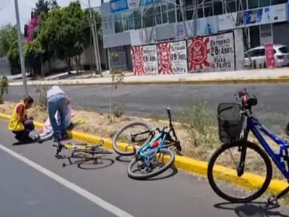 Dos hombres auxilian a uno de los ciclistas que fueron arrollados este domingo en Puebla.
