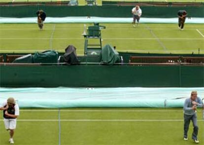 Trabajadores del torneo de Wimbledon extienden lonas sobre el césped de unas pistas del complejo tenístico.