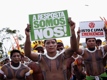 Dos indígenas brasileños levantan carteles con las frases "¡La respuesta somos nosotros!" y "Esto es una emergencia", durante una manifestación en Brasilia, el 24 de abril de 2024.
