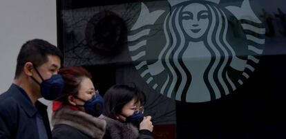 Varias personas con mascarillas pasan por delante de un establecimiento de Starbucks en la ciudad china de Beijing.