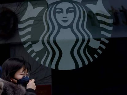 Varias personas con mascarillas pasan por delante de un establecimiento de Starbucks en la ciudad china de Beijing.