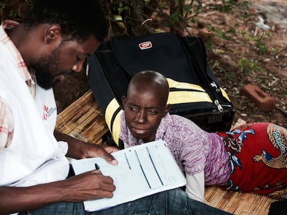 Las lesiones que ha provocado el cáncer de cuello uterino en Emily Mkumba le impiden sentarse. Ella permanece tumbada mientras escucha a un enfermero del equipo de paliativos de MSF en su casa de una aldea de Malawi.