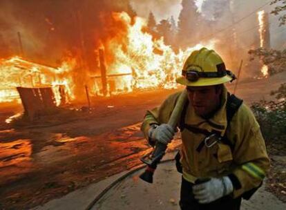 Un bombero arrastra una manguera ante viviendas en llamas en la localidad californiana de Running Springs