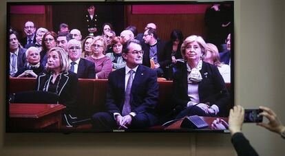 L'exconsellera Joana Ortega, l'expresident Artur Mas i l'exconsellera Irene Rigau, fotografiats a través de la pantalla de televisió que retransmet la vista.