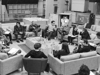 O produtor, diretor e roteirista J.J. Abrams (com óculos, no centro) e a partilha de 'Star Wars: Episode VII' nos Estudios Pinewood, Reino Unido (desde Abrams, no sentido das agulhas do relógio): Harrison Ford, Daisy Ridley, Carrie Fisher, Peter Mayhew, o produtor Bryan Burk, a presidenta de Lucasfilm e produtora Kathleen Kennedy, Domhnall Gleeson, Anthony Daniels, Mark Hamill, Andy Serkis, Oscar Isaac, John Boyega, Adam Driver e o roteirista Lawrence Kasdan.