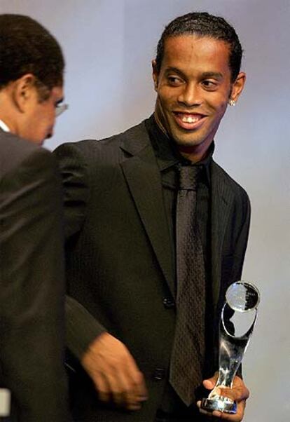 Ronaldinho sonríe a Eusebio tras recibir de éste su trofeo.