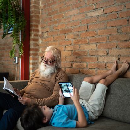 Grandfather reading and book and grandson using digital tablet at home