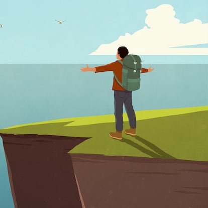Carefree male backpacker standing with arms outstretched at cliff's edge over sunny ocean