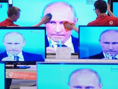 Funcionários de uma loja limpam uma tela de televisão durante pronunciamento do presidente Vladimir Putin, na quinta-feira, em Moscou.