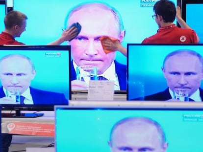 Funcionários de uma loja limpam uma tela de televisão durante pronunciamento do presidente Vladimir Putin, na quinta-feira, em Moscou.