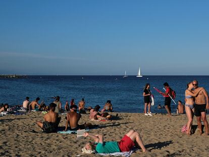Una mujer besa a un hombre mientras disfrutan del clima soleado en la playa de la Barceloneta.