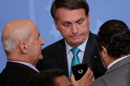 El presidente Jair Bolsonaro mira el móvil del ministro Luiz Eduardo Ramos en un acto en el Palacio del Planalto.