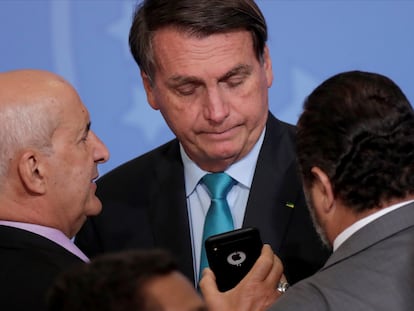 El presidente Jair Bolsonaro mira el móvil del ministro Luiz Eduardo Ramos en un acto en el Palacio del Planalto.