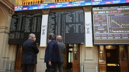 Tres hombres observan los valores económicos de la Bolsa de Madrid.