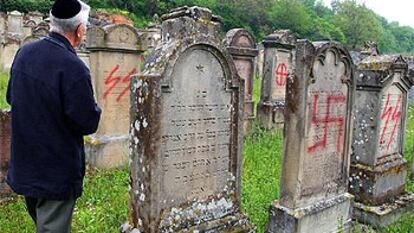 Un hombre  observa el estado de algunas lápidas del cementerio de Herrlisheim, pintadas con signos nazis.