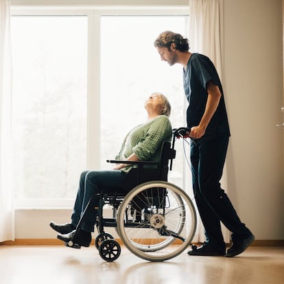 Full length side view of male nurse pushing disabled senior woman on wheelchair in alley at retirement home