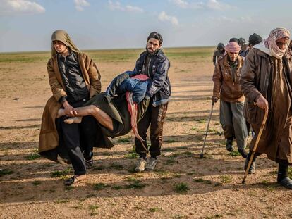 Varios hombres, sospechosos de pertenecer al Estado Islámico, sujetan un herido, mientras avanzan hacia las Fuerzas Democráticas Sirias, lideradas por los kurdos, tras abandonar Baghouz, en la provincia de Deir Ezzor, al norte de Siria.