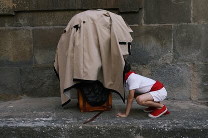Un niño mira dentro de la manta que cubre un "Cabezudo" tendido en el suelo durante la "Comparsa de gigantes y cabezudos" del festival de San Fermín.