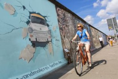 Una ciclista pasa por delante de la East Side Gallery, en Berlín, un tramo original del Muro de Berlín dedicado ahora al arte urbano.