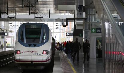 Viajeros en las escaleras mecánicas con sus maletas y un AVE en la estación de Atocha de Madrid.