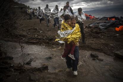 Un refugiado anda con su hijo en la playa de Lesbos después de llegar con una barcaza desde Turquía, el 24 de octubre de 2015. La UE ha pedido a Turquía que atienda mejor a los dos millones de refugiados que alberga en su territorio.