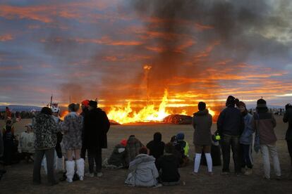 Los llamados "burners" miran una obra de arte que arde a la vez que amanece en el desierto.