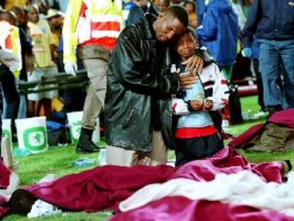 Un hombre y un niño, arrodillados sobre el césped, lloran junto a varios cadáveres.