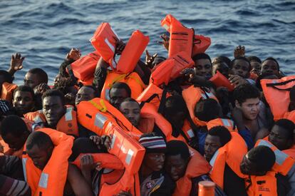 Una multitud de personas se amontona en un bote de goma para colocarse el chaleco salvavidas. 