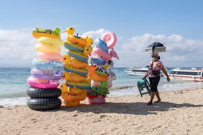 Una vendedora ambulante de comida pasa ante las pilas de flotadores en la playa desierta de Sanur, Bali, Indonesia, este miércoles. El Gobierno indonesio ha planeado reabrir las islas de Bali a los turistas extranjeros para finales de julio de 2021.