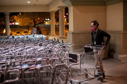 Un hombre con mascarilla apila carritos de supermercado.
