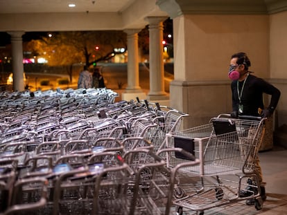 Un hombre con mascarilla apila carritos de supermercado.