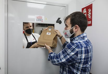 Juan Beltrán le entrega un pedido de FoodCraft a su socio, Juan Diego Gaitán, que se lo llevará a un repartidor que espera en la puerta del local en Tetuán donde está su cocina.