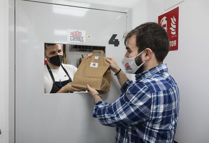 Juan Beltrán le entrega un pedido de FoodCraft a su socio, Juan Diego Gaitán, que se lo llevará a un repartidor que espera en la puerta del local en Tetuán donde está su cocina.