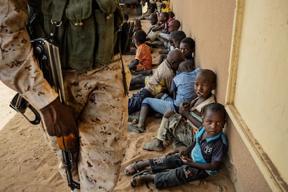 Un militar de las Fuerzas Armadas Nigerinas vigila en los alrededores de la escuela de la aldea de Inizdan, en el oeste de Níger, mientras los niños se refugian del calor a la sombra de sus paredes y esperan a sus padres, que participan en una reunión con agentes del Gobierno.