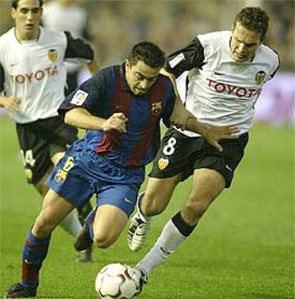 Xavi (izqda.) pugna por el balón con el valencianista Baraja.