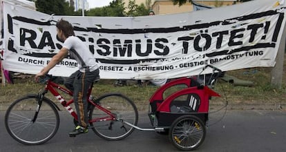 Un vecino pasa por una pancarta que dice &quot;El racismo mata&quot; montada delante del nuevo centro de refugiados en Berl&iacute;n este mi&eacute;rcoles.
