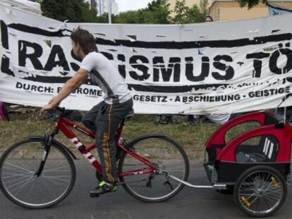 Un vecino pasa por una pancarta que dice &quot;El racismo mata&quot; montada delante del nuevo centro de refugiados en Berl&iacute;n este mi&eacute;rcoles.