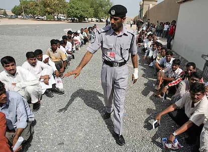 Un policía obliga a colocarse en el suelo a trabajadores, la mayoría asiáticos, que hacen cola frente a la oficina de inmigración de Dubai.