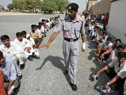 Un policía obliga a colocarse en el suelo a trabajadores, la mayoría asiáticos, que hacen cola frente a la oficina de inmigración de Dubai.