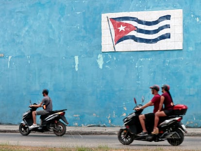 Motociclistas cruzan frente a un mural con la bandera cubana este miércoles en La Habana.