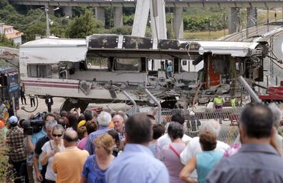 Un grupo de personas contempla las labores de retirada de uno de los vagones del tren Alvia procedente de Madrid que descarriló ayer a la altura de Santiago de Compostela