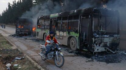 Un home passa amb moto pel costat d'un dels autobusos calcinats a Idlib quan es dirigien a evacuar els civilis de Fua i Kefraia.